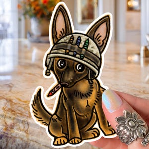 May include: A sticker featuring a cartoon German Shepherd dog wearing a camouflage helmet with colorful accents. The dog is depicted with a cigarette in its mouth, and the sticker has a white border.