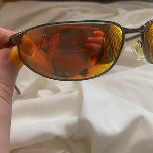 May include: Brown metal frame sunglasses with orange mirrored lenses. The Ray-Ban logo is visible on the right lens.