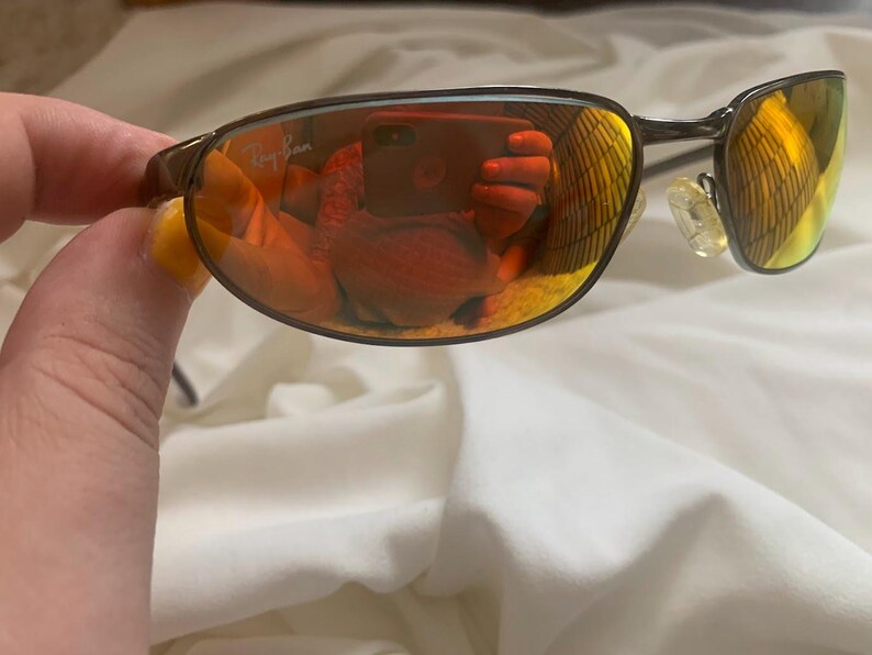 May include: Brown metal frame sunglasses with orange mirrored lenses. The Ray-Ban logo is visible on the right lens.