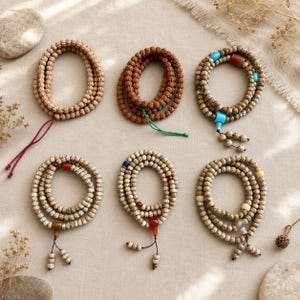 May include: Six circular prayer bead necklaces arranged in two rows. The beads vary in colour and texture, including light brown, dark brown, and speckled tan wood. Some necklaces feature accent beads in turquoise, red, and cream, with dangling ends.