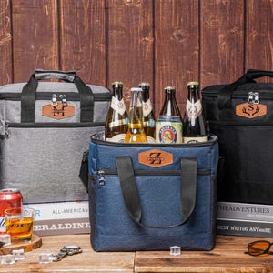 May include: Three insulated cooler bags in gray, black, and blue, each with a handle and a zippered top. The bags are filled with beer bottles. The blue bag has a brown leather patch with the letter "Z".
