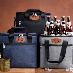 May include: Three insulated cooler bags in black, navy blue, and gray, each featuring a brown leather patch with personalized text: NICK, SBN, and KIA. The bags have black handles, zippers, and side pockets, and are surrounded by beer bottles.
