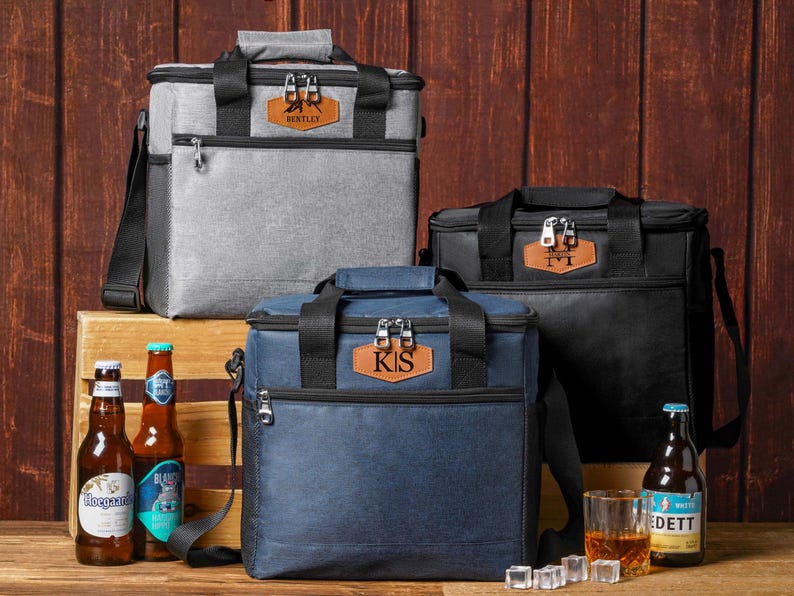 May include: Three square insulated cooler bags in gray, navy blue, and black, each featuring a front zippered pocket, black carrying handles, and a brown leather-like patch with personalized text including BENTLEY, KS, and M.
