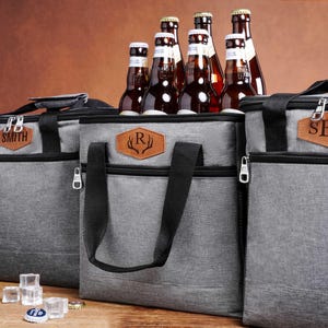 May include: Three grey insulated cooler bags with black straps and zippers. Each bag features a brown leather-like patch with personalized text: SMITH, an R with antlers, and SBN. Several brown glass beer bottles are tucked inside the bags.