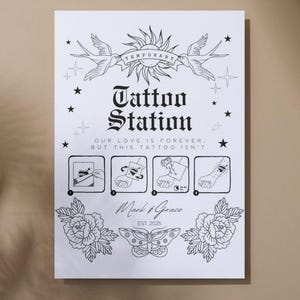 以下が含まれることがあります： 黒いイラストとテキストが描かれた白いサイン。 「Tattoo Station」の文字が中央に配置され、その下に「OUR LOVE IS FOREVER, BUT THIS TATTOO ISN'T.」というフレーズがあります。 太陽、鳥、星、花、蝶が含まれています。