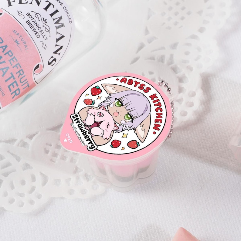 Puede incluir: Un recipiente de pl&aacute;stico rosa y blanco con un personaje de dibujos animados en la tapa. El personaje es un zorro rosa con pelaje blanco y ojos verdes. El recipiente tiene el texto "ABYSS KITCHEN" y "Strawberry" en la tapa.