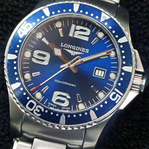 May include: A stainless steel Longines watch with a blue dial and bezel. The watch features silver hands and markers, with the number 12, 9, and 6 prominently displayed. The bezel has white markings and the watch is on a stainless steel band.