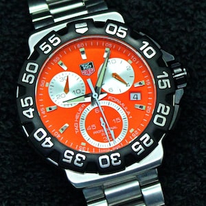 May include: A white ceramic mug with a black handle and the text "But First, Coffee" in a bold, black font. The mug is set against a blurred background, suggesting a cozy setting.