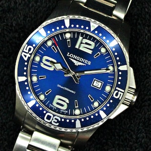 May include: A stainless steel Longines wristwatch with a blue dial and a matching blue rotating bezel. The watch features large silver-tone numerals at the 6 and 12 o'clock positions, a date window at 3 o'clock, and luminous markers on the dial.