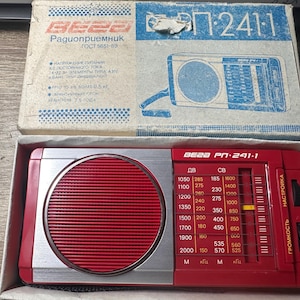 Peut inclure: Un récepteur radio vintage rouge et argent, modèle BECO PN-241-1, avec une grille de haut-parleur rouge et un cadran de réglage. La radio est dans sa boîte d'origine, avec du texte et des graphiques bleus et blancs. La boîte est ouverte.