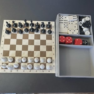 以下が含まれることがあります： チェス盤と白黒の駒、ドミノとサイコロが入ったボードゲームセット。チェス盤は茶色と白です。サイコロは赤と黒です。ドミノは白と黒です。