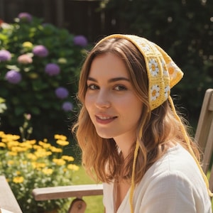 May include: A yellow crochet headscarf with white daisy accents. The headscarf is tied at the back and is worn by a person. The background features a garden with flowers and a wooden chair.