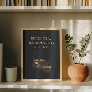 Puede incluir: Una impresión enmarcada con un fondo azul oscuro y texto blanco que dice "Drink tea. Read poetry. Repeat." Una ilustración estilizada de una tetera y una taza de té con una flor está en el centro de la impresión.