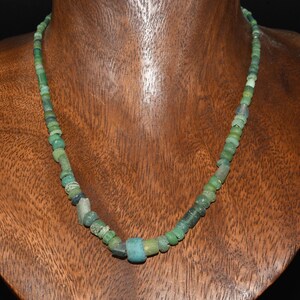 May include: A necklace composed of numerous small, irregularly shaped beads in various shades of green, ranging from pale mint to deep forest green. The beads vary in size and texture, featuring a mix of cylindrical, spherical, and disc shapes.