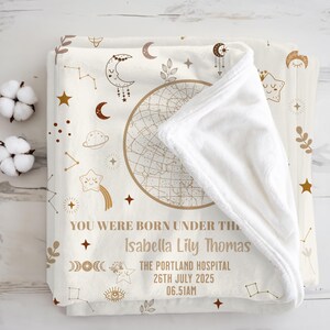 Peut inclure: Couverture de bébé crème avec un motif céleste. Elle présente une carte des étoiles, des étoiles, des lunes et le texte "YOU WERE BORN UNDER THE Isabella Lily Thomas THE PORTLAND HOSPITAL 26TH JULY 2025 06.51AM".
