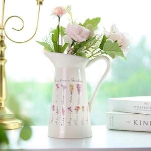 Könnte beinhalten: Ein weißer Keramik-Krug mit einem Blumendesign und dem Text "Grandma's Garden". Der Krug hat einen Henkel und einen Ausguss. Er ist mit rosa und weißen Blumen gefüllt.
