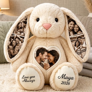 Può includere: Un coniglio di peluche color crema con lunghe orecchie cadenti che presentano fotografie stampate di coppie. Una foto a forma di cuore di una coppia si trova sul petto. I piedi sono ricamati con il testo "Love you Always" e "Maya 2026" in nero.