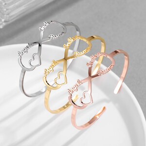 Puede incluir: Tres pulseras doradas con símbolos de infinito y recortes en forma de corazón. Cada pulsera tiene dos nombres inscritos: "Angela" y "Reanna".