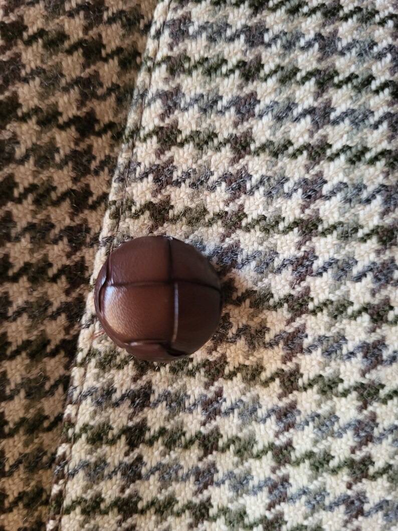 May include: Close-up of a brown leather button on a houndstooth patterned fabric. The fabric features a repeating pattern in shades of brown, gray, and cream. The button is round and has a textured surface.