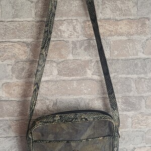 May include: A green and brown snakeskin-patterned crossbody bag with a gold-tone floral embellishment. The bag has a zipper closure and a long adjustable strap.
