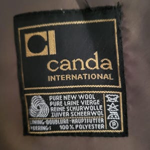 May include: A black label with gold lettering and a gold square logo that reads "CI canda INTERNATIONAL". The label also states "PURE NEW WOOL" and "100% POLYESTER".