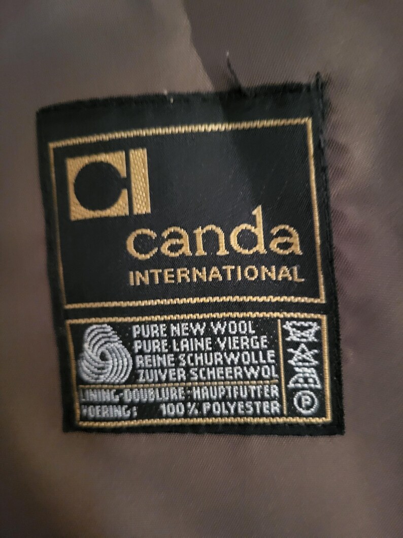 May include: A black label with gold lettering and a gold square logo that reads "CI canda INTERNATIONAL". The label also states "PURE NEW WOOL" and "100% POLYESTER".