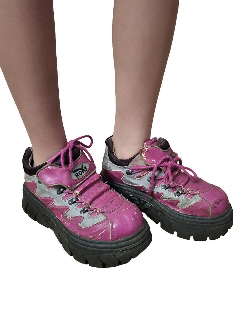 May include: A pair of pink and gray platform sneakers with black soles. The sneakers have a chunky design, pink laces, and the brand name "ROXY" is visible on the side. The shoes show signs of wear.