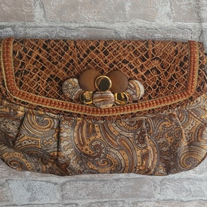 Puede incluir: Un bolso de mano de color marrón y dorado con estampado de paisley, solapa de piel de serpiente y detalles de botones dorados y marrones.