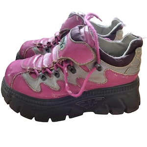 May include: A pair of pink and gray platform sneakers with black soles. The shoes have pink laces and a chunky design, showing signs of wear. The sneakers have a retro, grunge aesthetic.