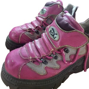 May include: A pair of well-worn, pink and gray Roxy platform boots. The boots have a chunky black sole, pink laces, and the Roxy logo on the side. The leather shows signs of wear and tear.