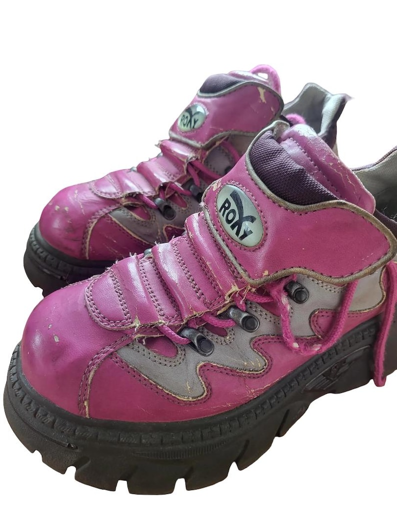 May include: A pair of well-worn, pink and gray Roxy platform boots. The boots have a chunky black sole, pink laces, and the Roxy logo on the side. The leather shows signs of wear and tear.
