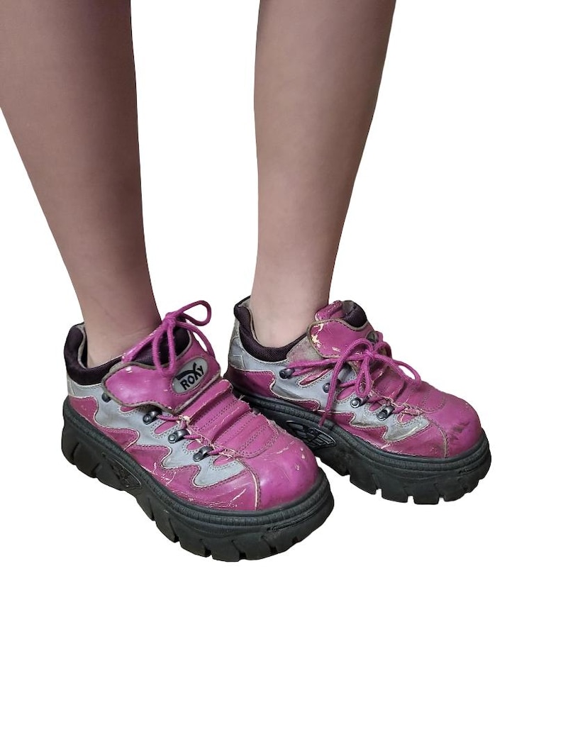 May include: A pair of pink and silver Roxy platform sneakers. The sneakers have a chunky black sole, pink laces, and the Roxy logo on the side. The shoes show signs of wear.
