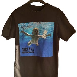May include: Black t-shirt with the Nirvana "Nevermind" album art. The image depicts a baby underwater, reaching for a dollar bill. The band name and album title are printed in blue at the bottom of the graphic.