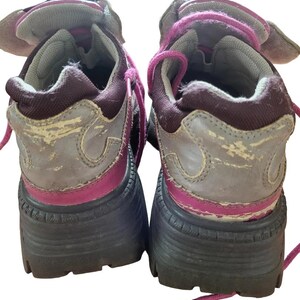 May include: Pair of worn, chunky platform sneakers. The shoes feature a gray and burgundy color scheme with pink laces and accents. The soles are thick and black, and the uppers show signs of wear.