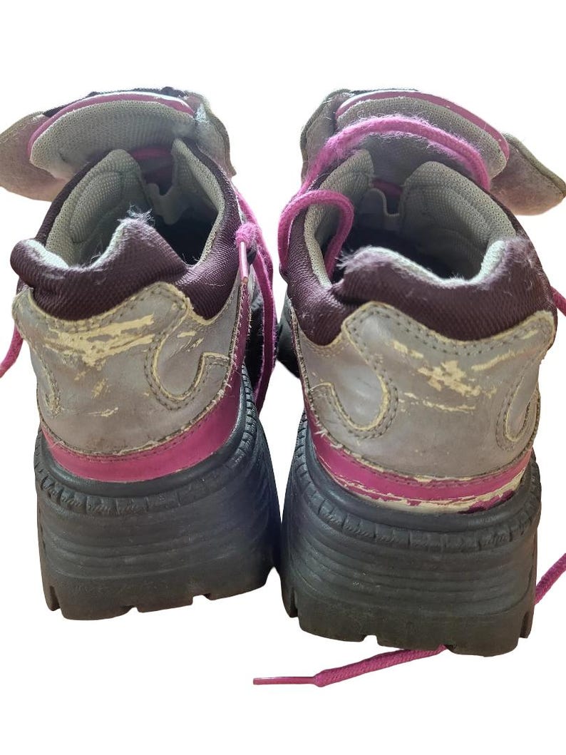 May include: Pair of worn, chunky platform sneakers. The shoes feature a gray and burgundy color scheme with pink laces and accents. The soles are thick and black, and the uppers show signs of wear.