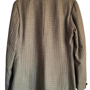 May include: A houndstooth blazer in shades of brown and black, viewed from the back. The jacket has a notched collar and a two-button closure. The blazer is hanging on a purple hanger.
