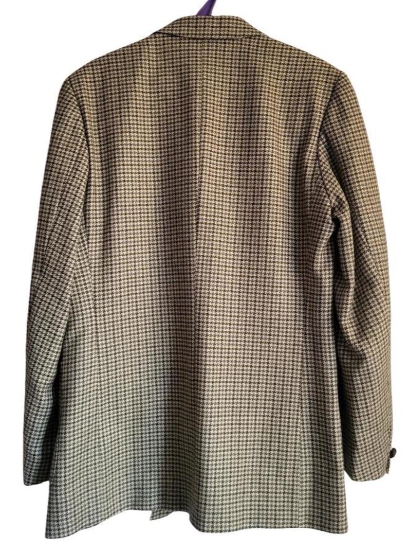 May include: A houndstooth blazer in shades of brown and black, viewed from the back. The jacket has a notched collar and a two-button closure. The blazer is hanging on a purple hanger.