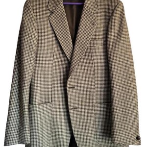May include: A houndstooth patterned blazer in shades of brown and white, hanging on a purple hanger. The jacket features a notched lapel, two front pockets, and a two-button closure. The interior lining is a dark brown color.