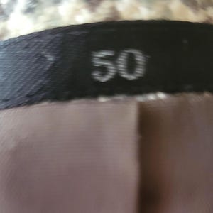 May include: Close-up of a garment label with the number "50" printed in white on a black background. The label is sewn onto a brown fabric, with a patterned fabric visible above.
