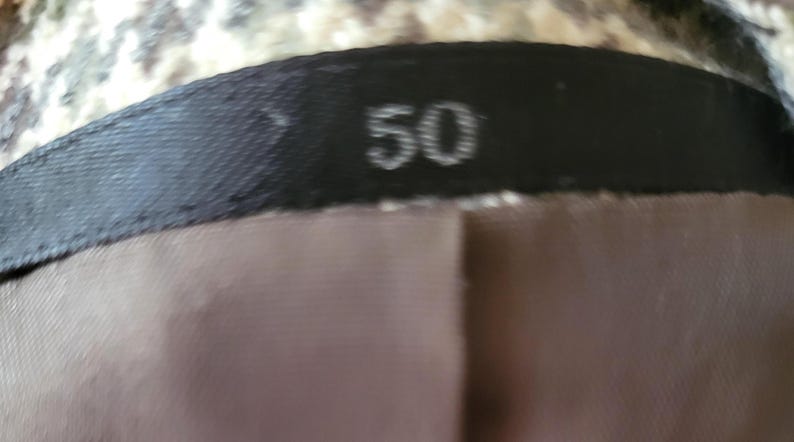 May include: Close-up of a garment label with the number "50" printed in white on a black background. The label is sewn onto a brown fabric, with a patterned fabric visible above.