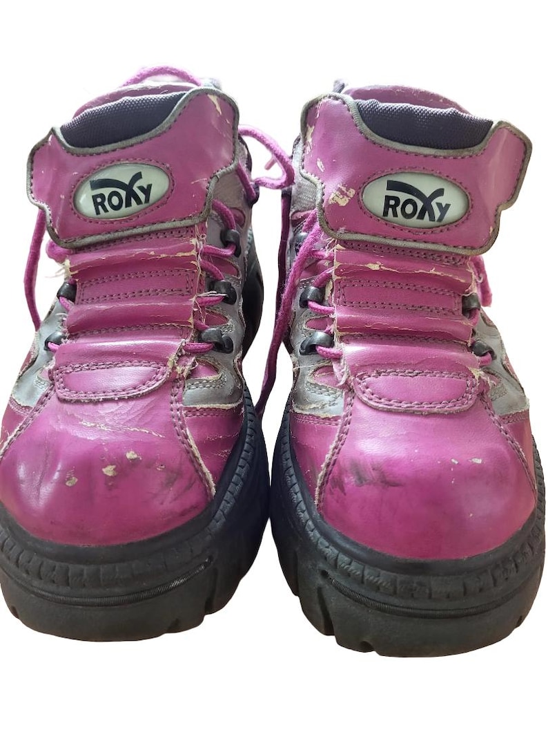 May include: Pair of well-worn, pink and gray Roxy high-top boots. The boots have a chunky black sole, pink laces, and the Roxy logo on the side. The leather shows signs of wear and tear.