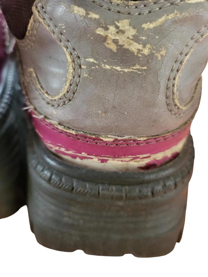 May include: Close-up of a worn brown boot with a thick, dark sole. The boot's upper shows signs of wear and tear, with peeling paint revealing a pink layer beneath. The stitching is visible along the edges.