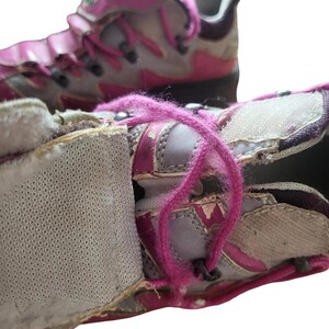 May include: Close-up of a pair of worn athletic shoes. The shoes are primarily gray and pink, with pink laces and accents. The shoes have a hook-and-loop closure and show signs of wear and tear.