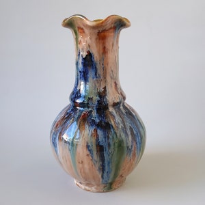 Puede incluir: Un jarrón de cerámica con un borde festoneado y un cuerpo bulboso. El jarrón está decorado con un esmalte colorido en tonos de azul, verde, marrón y blanco.