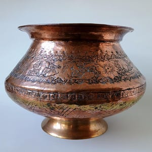 Peut inclure: Un bol décoratif en cuivre avec des gravures florales et géométriques détaillées. Le bol présente un large bord, un corps arrondi et un socle. Le cuivre vieilli a une teinte riche et chaude, avec des signes d'usure.