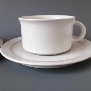 K&ouml;nnte beinhalten: Ein wei&szlig;es Porzellan-Teetassen-Set. Die Tasse hat ein schlichtes Design und einen abgerundeten Henkel. Die Untertasse ist etwas gr&ouml;&szlig;er als die Tasse und hat eine glatte, wei&szlig;e Oberfl&auml;che.