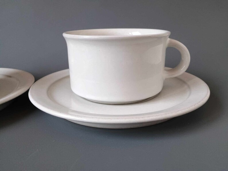 K&ouml;nnte beinhalten: Ein wei&szlig;es Porzellan-Teetassen-Set. Die Tasse hat ein schlichtes Design und einen abgerundeten Henkel. Die Untertasse ist etwas gr&ouml;&szlig;er als die Tasse und hat eine glatte, wei&szlig;e Oberfl&auml;che.