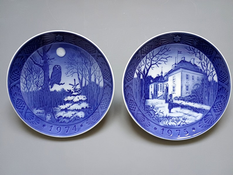Puede incluir: Dos platos decorativos azules y blancos. Uno presenta un b&uacute;ho en una escena de bosque con luna llena y el a&ntilde;o 1974. El otro representa un edificio y el a&ntilde;o 1975.
