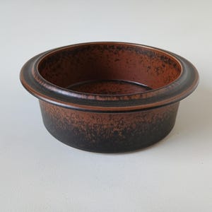 May include: A round, brown ceramic bowl with a wide rim. The bowl has a textured surface with a gradient from dark brown to lighter brown. The rim is a darker shade of brown.