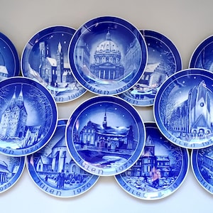 May include: A collection of ten blue and white ceramic Christmas plates featuring various scenes of churches and buildings. The plates are decorated with the word "Julen" and the year of each plate, ranging from 1969 to 1981.